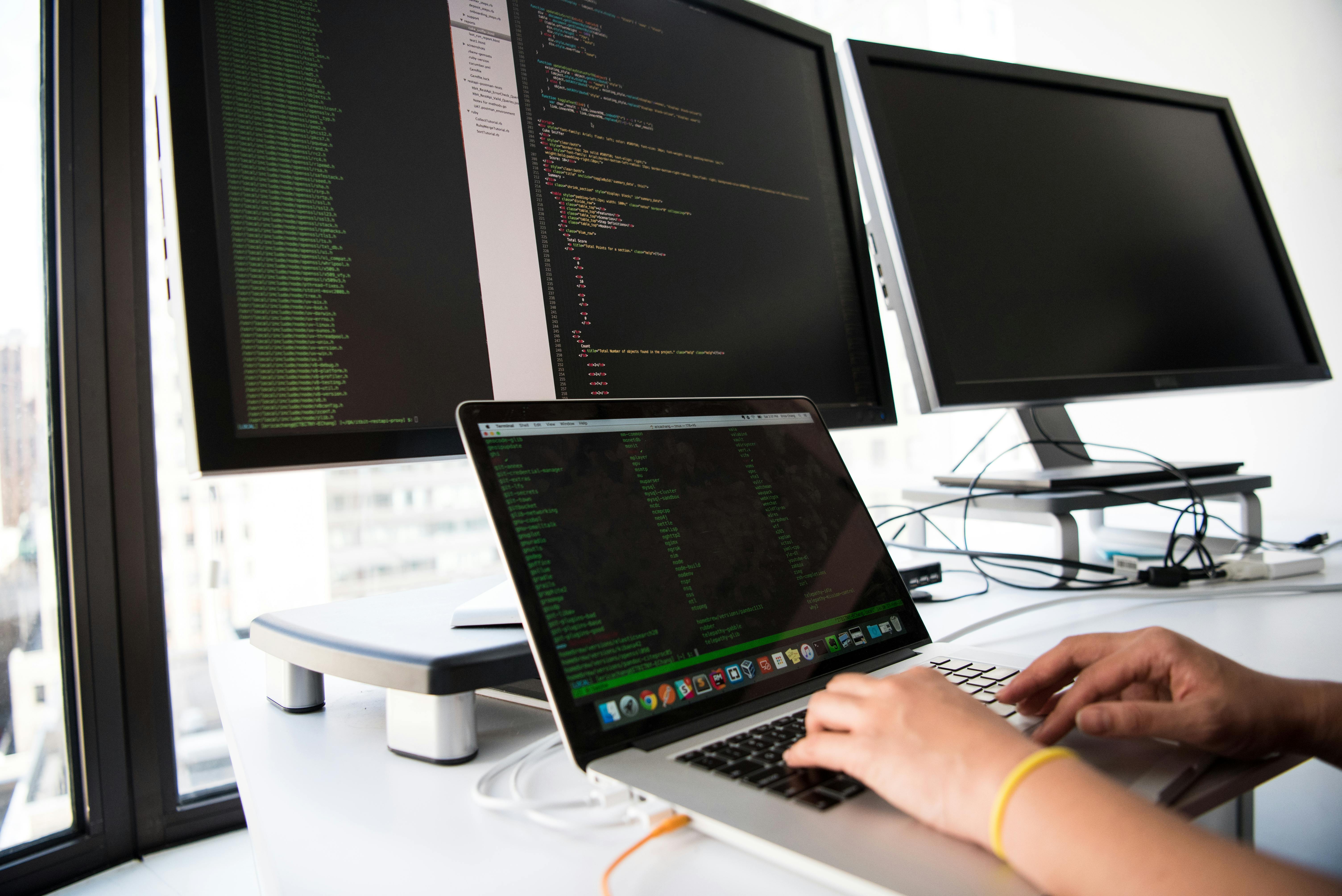several computer screens set up on a white desk looking at coding