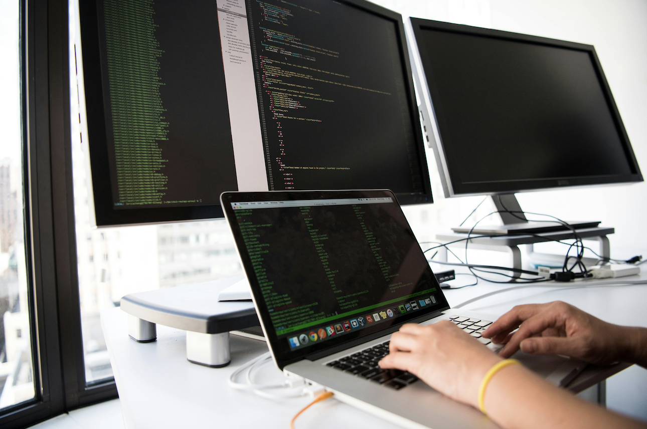 person working on code with 3 computer screens